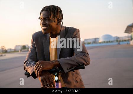 Smiling young businessman with electric push scooter on street Stock Photo