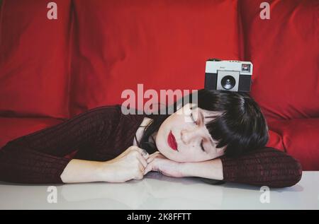 Woman resting on table with analog camera in front of red couch Stock Photo