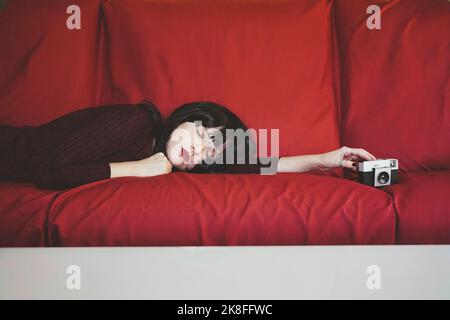 Woman with analog camera relaxing on red couch Stock Photo