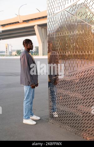 Young businessman looking at reflection on metal wall Stock Photo