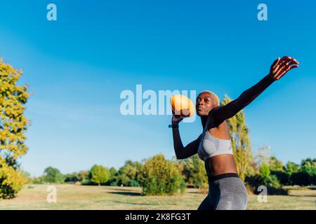 Young sportswoman throwing American football in field Stock Photo