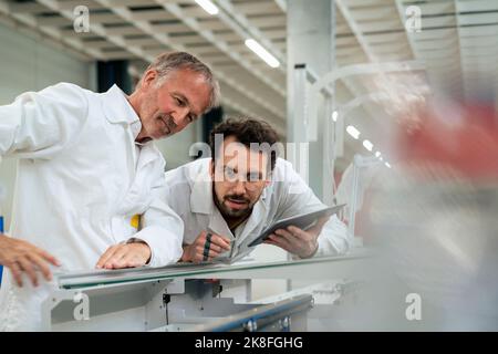 Engineer holding tablet PC examining machinery with colleague at industry Stock Photo