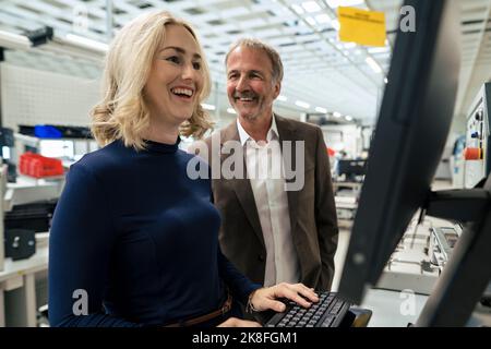 Happy businesswoman using computer standing by colleague at industry Stock Photo