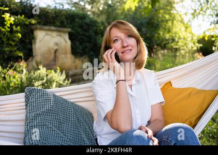 Woman talking through mobile phone sitting in hammock at garden Stock Photo