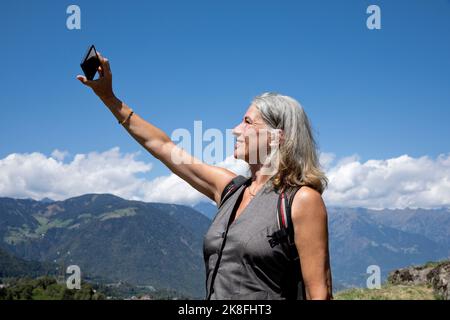 Smiling senior woman taking selfie through smart phone on sunny day Stock Photo