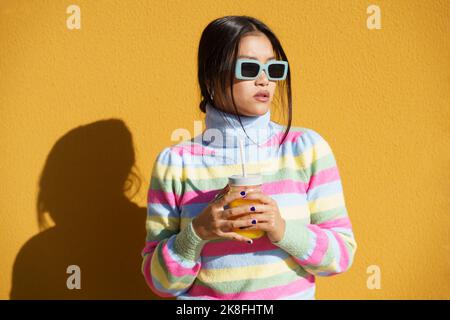Young woman standing with orange juice in front of wall Stock Photo