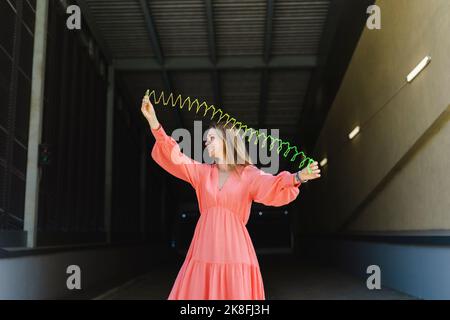 Happy woman stretching coiled spring toy on footpath Stock Photo