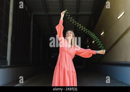 Happy woman playing with metal coil toy on footpath Stock Photo