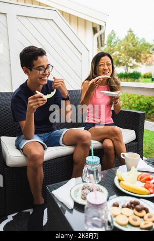 Happy woman enjoying snacks with son on couch at porch Stock Photo