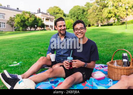 Happy boy enjoying picnic with father sitting in lawn Stock Photo