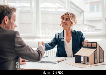 Businesswoman by house model shaking hands with client at office Stock Photo