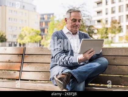 Senior man using tablet computer sitting on bench Stock Photo