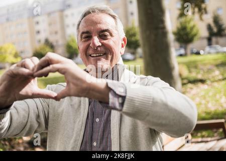 Smiling senior man making heart shape with hand Stock Photo