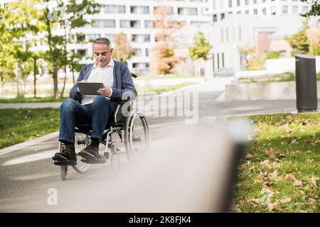Senior man using tablet PC sitting on wheelchair Stock Photo