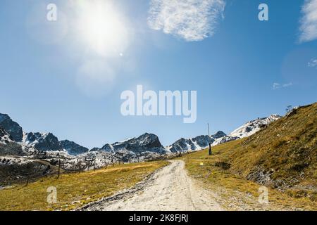 Dirt road leading towards snowcapped mountains on sunny day Stock Photo