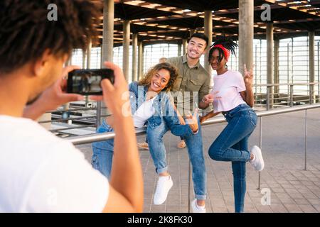 Young man photographing friends through smart phone at railroad station Stock Photo