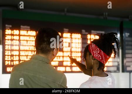 Young woman talking to friend and pointing at departure board Stock Photo