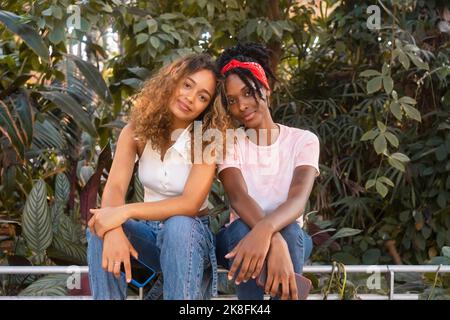 Young multiracial friends sitting together in front of plants Stock Photo