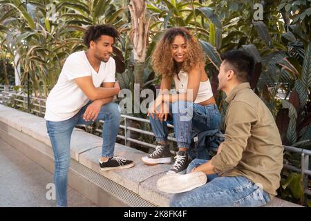 Smiling woman talking to multiracial friends on wall Stock Photo