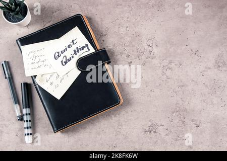 Quiet Quitting. Top view to desk with office supplies. Sticky note with written text Quiet Quitting on closed paper business notebook planner. Quiet Stock Photo