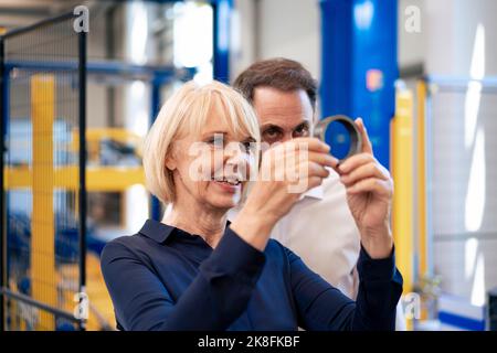 Smiling senior businesswoman with businessman analyzing machine part in industry Stock Photo