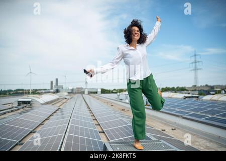 Happy businesswoman standing on one leg at rooftop with solar panels Stock Photo