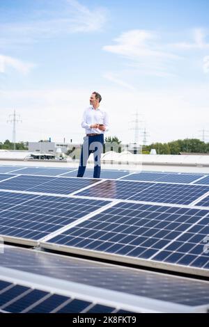 Businessman standing by solar panels on rooftop Stock Photo