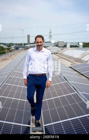Mature businessman walking amidst solar panels on rooftop Stock Photo