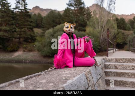 Young woman wearing tiger mask sitting on wall Stock Photo