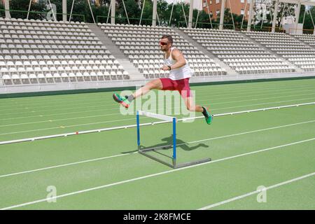 Athlete jumping over hurdle on sports track Stock Photo