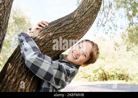 Smiling boy hugging tree branch in park Stock Photo