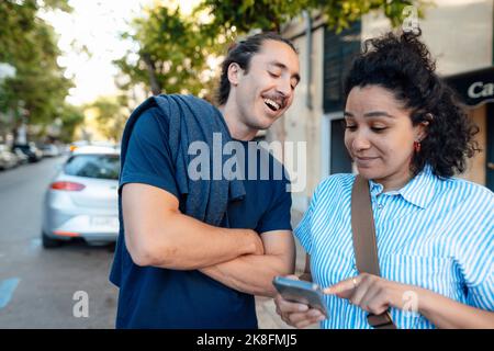 Happy man looking at girlfriend using mobile phone on street Stock Photo