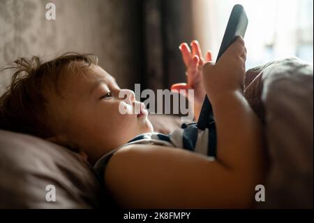 Baby boy using mobile phone lying in bed Stock Photo