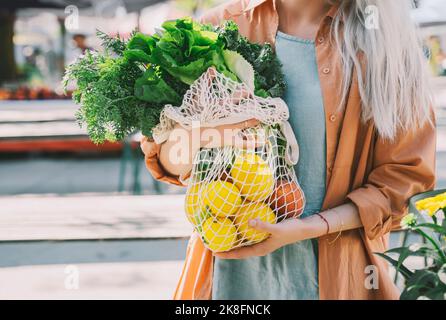 Customer holding leafy vegetables and lemons in mesh bag at local market Stock Photo