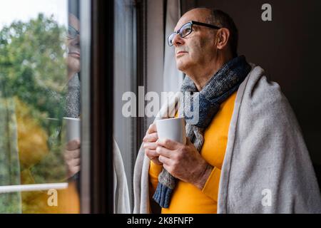 Thoughtful man with tea looking out of window at home Stock Photo