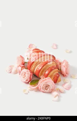 Pink rose petals around croissant on white background Stock Photo