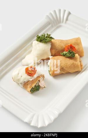 Stuffed shrimp crepes garnished with tomato and cream arranged in tray against white background Stock Photo