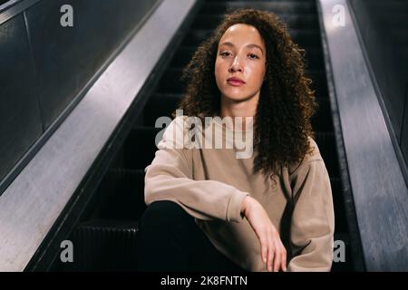 Young woman sitting on escalator Stock Photo