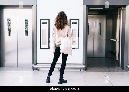 Woman with curly hair standing in front of elevator Stock Photo