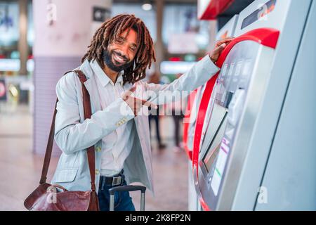 Happy businessman with luggage pointing at ticket machine in station Stock Photo