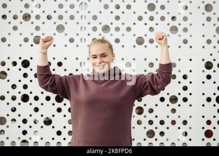 Smiling woman making fists in front of wall Stock Photo