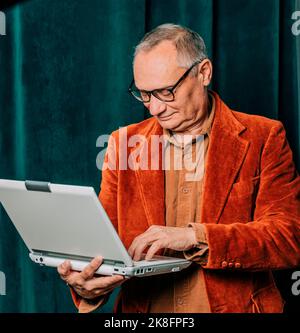 Senior man using laptop in front of curtain Stock Photo