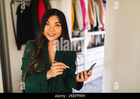 Happy young woman holding make-up brush standing at home Stock Photo