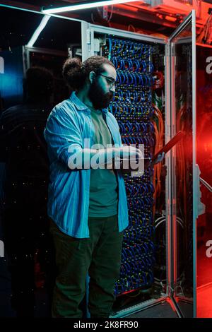IT engineer using laptop by servers in data center Stock Photo