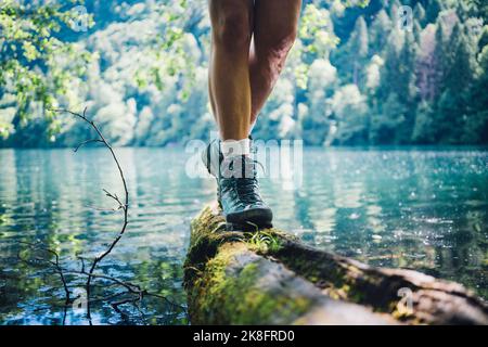 Woman wearing hiking boot walking on tree log by Lake Levico Stock Photo