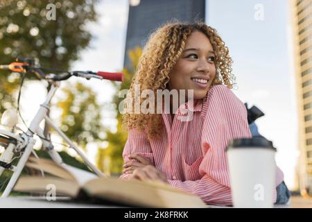Smiling curly haired woman contemplating on bench Stock Photo