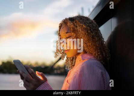 Young curly haired woman using smart phone at sunset Stock Photo