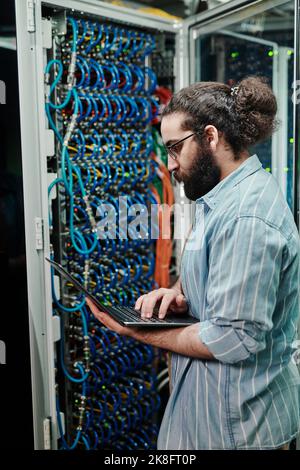 Technician configuring server through laptop in server room Stock Photo