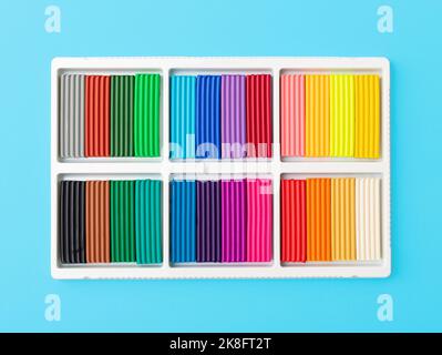 24 colors set of colorful plasticine sticks in white plastic packaging isolated on blue background. Pieces of multicolor plasticine modeling clay. Top Stock Photo