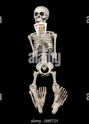 Skeleton holding a pair of playing cards on black background Stock Photo